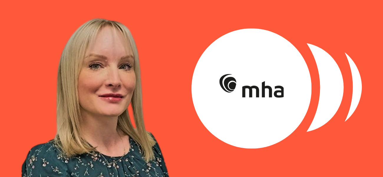 Smiling woman standing in front of an orange background, next to the MHA logo displayed inside a white circle.